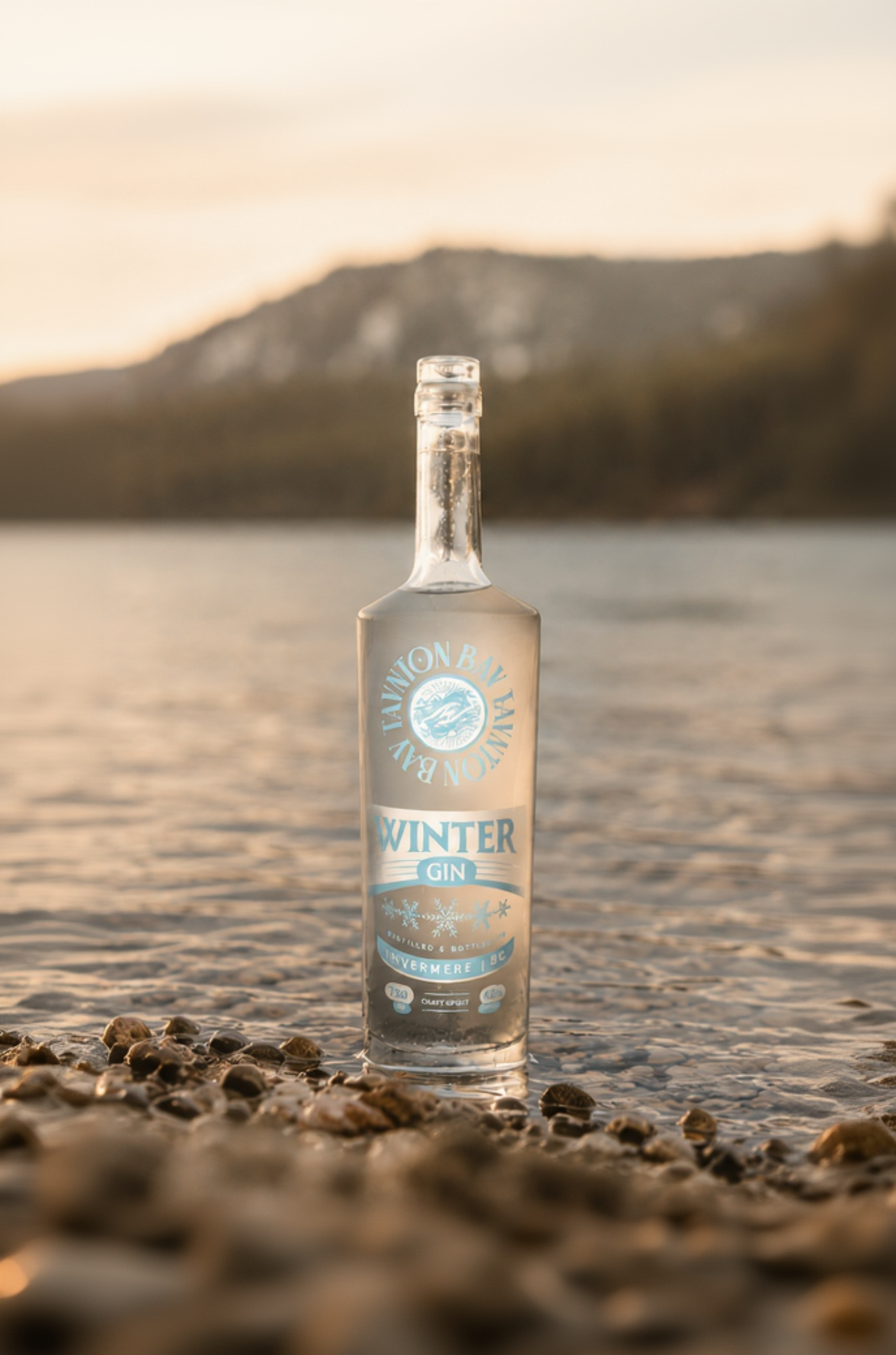 Bottle of 'Winter Gin' on a pebbly beach with a mountainous landscape in the background.